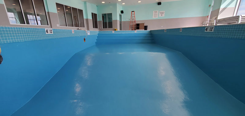 Empty indoor pool with blue tiles and a ladder in the background