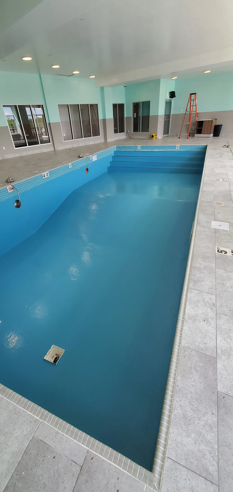 Indoor pool with tiled floor and walls, surrounded by construction materials.
